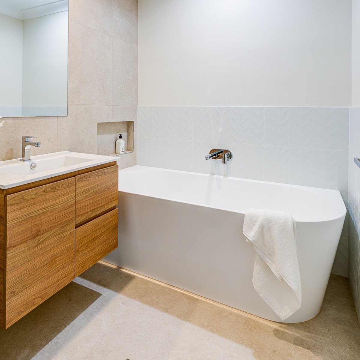 White back-to-corner bath beside a timber vanity