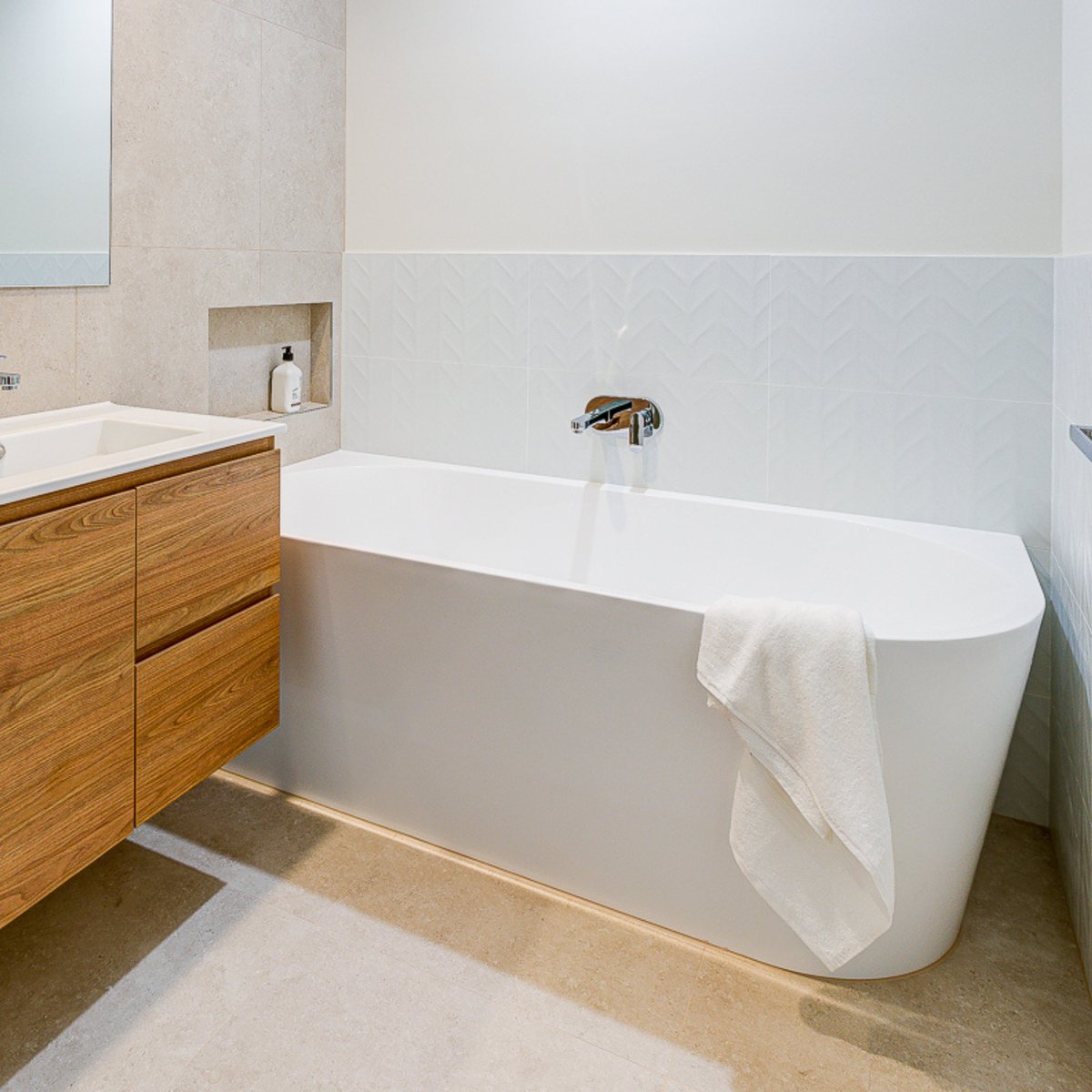 White back-to-corner bath beside a timber vanity