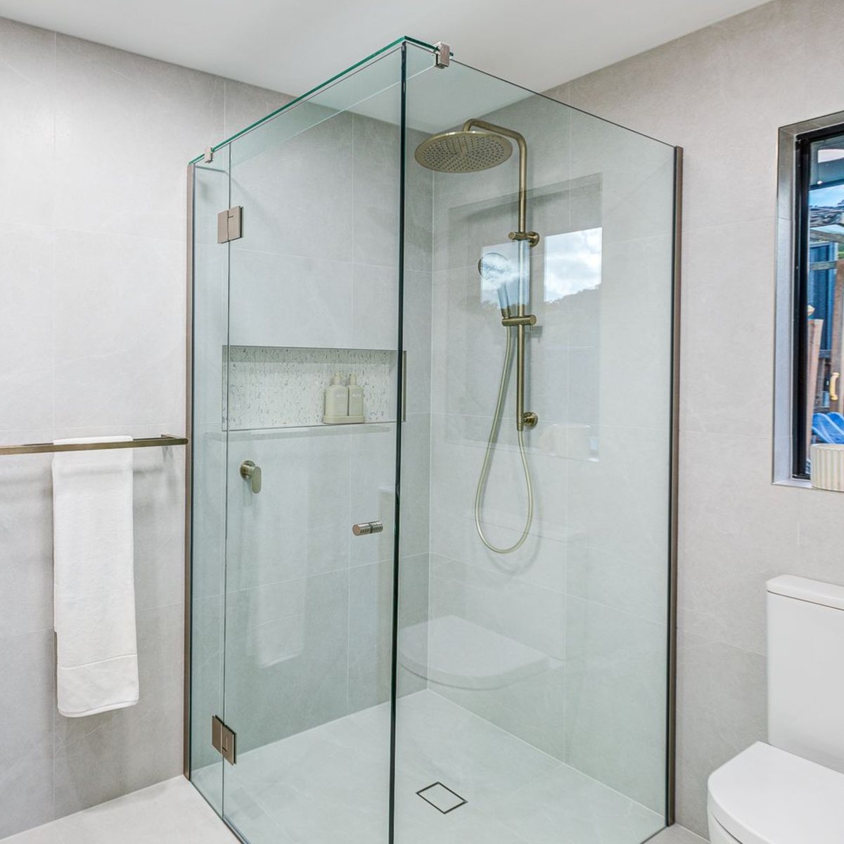 Frameless shower screen around a shower with a tiled niche